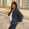 Femme portant une veste en jean avec de la broderie motifs cerise, avec un gobelet et une paille