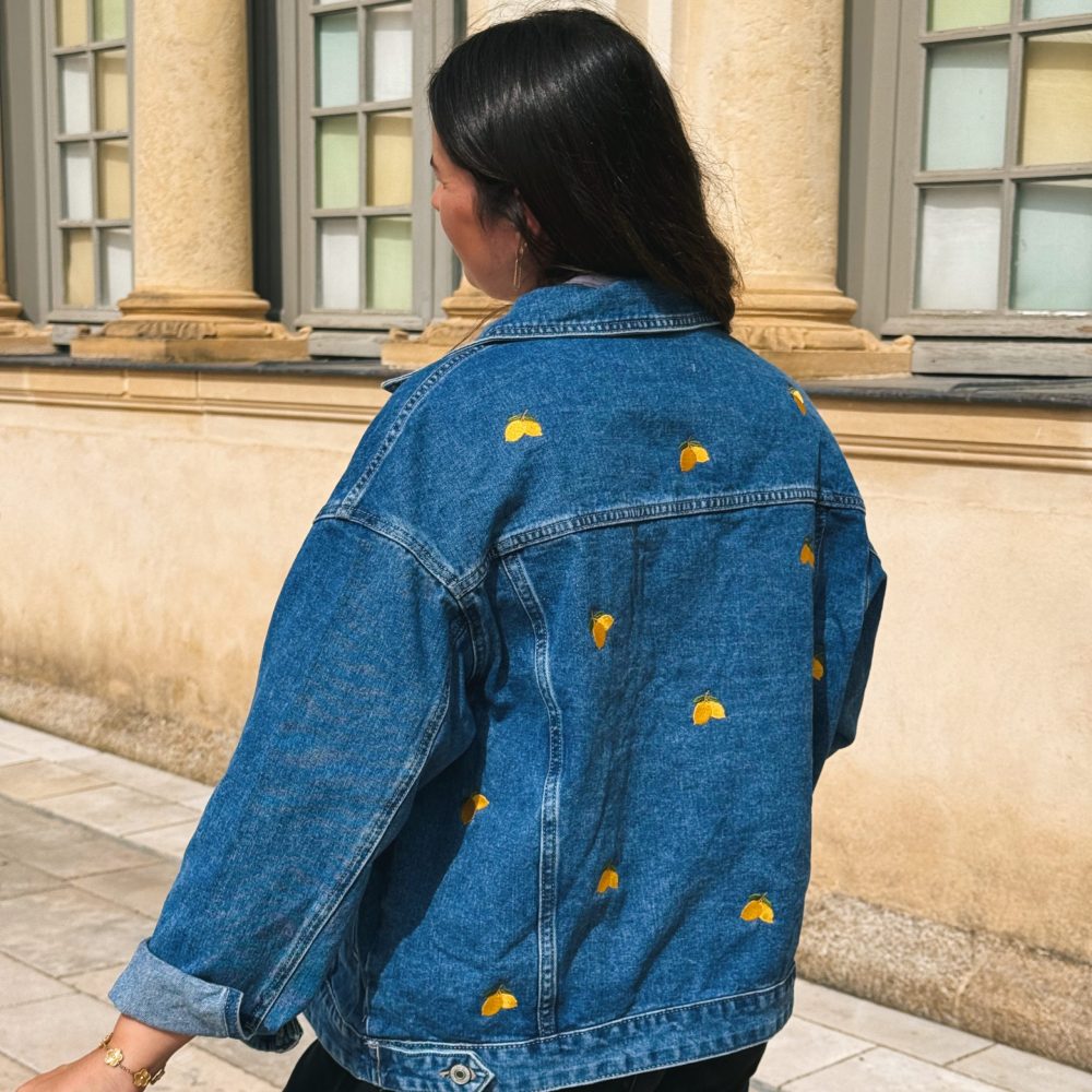 Femme de dos portant une veste en jean avec de la broderie motifs citron