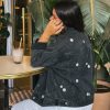Femme portant une veste en jean avec de la broderie motifs marguerites, sur un tabouret dans un bar