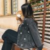 Femme portant une veste en jean avec de la broderie motifs marguerites, sur un banc en extérieur